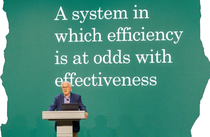 Photo of David Labaree presenting the opening keynote at BbT26 with the words 'A system in which efficiency is at odds with effectiveness' displayed behind him